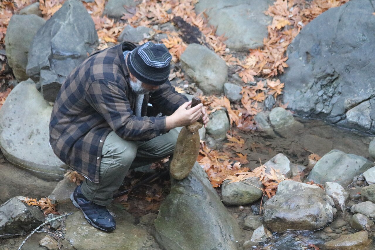 A man in a knit hat balances rocks near Swanson Creek in Uvas Canyon County Park, in Morgan Hill, California.